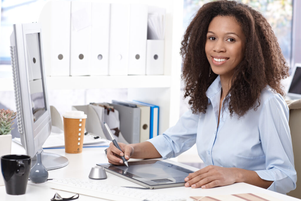 Professional woman working at desk with computer and tablet, preparing financial documents for small business loan application.