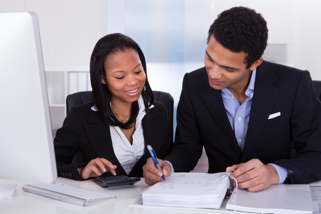 Two small business professionals reviewing financial documents together with a calculator and computer on the desk.